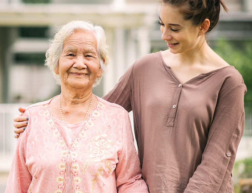 younger woman walking with an elderly woman - New Perspective Careers Assisted Living Careers