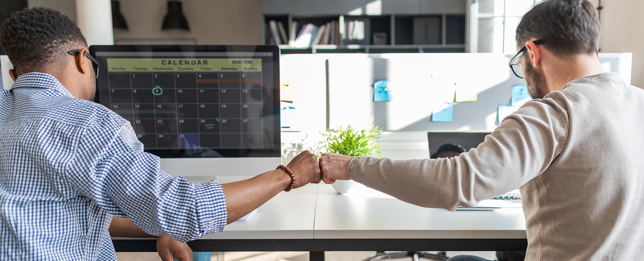 two men fist bumping each other at their desks - New Perspective Careers Assisted Living Careers